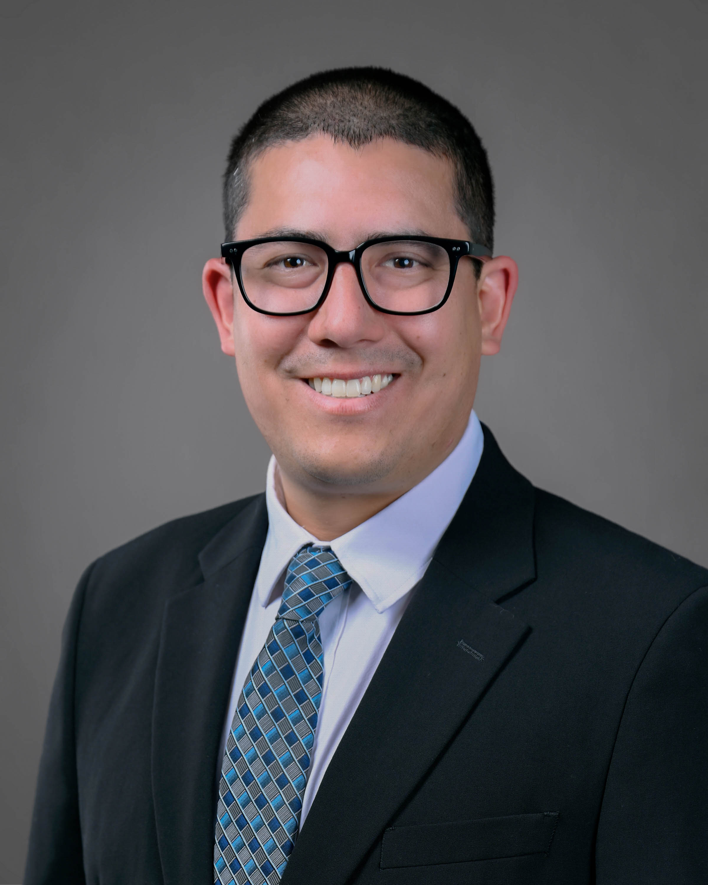 Smling short haired man with eyeglasses in a dark suit with a blue and dark grey tie